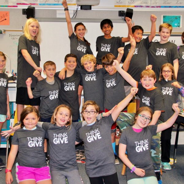 A team of students wearing ThinkGive t-shirts and raising their arms in the air, posing for the camera.