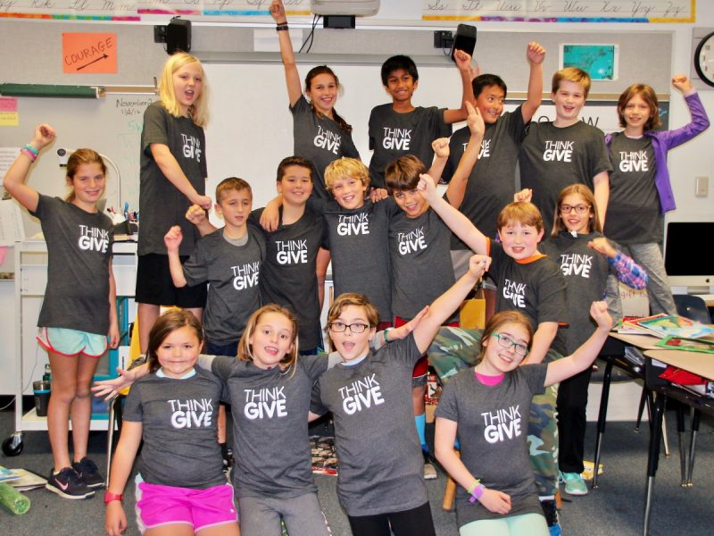 A team of students wearing ThinkGive t-shirts and raising their arms in the air, posing for the camera.