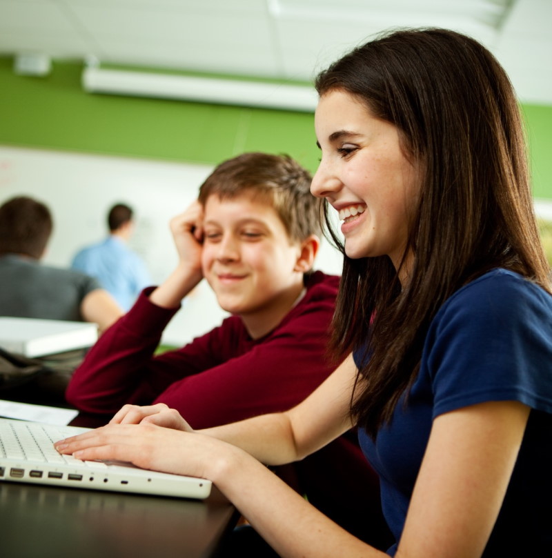 A boy and girl student smiling while reading an assignment together.